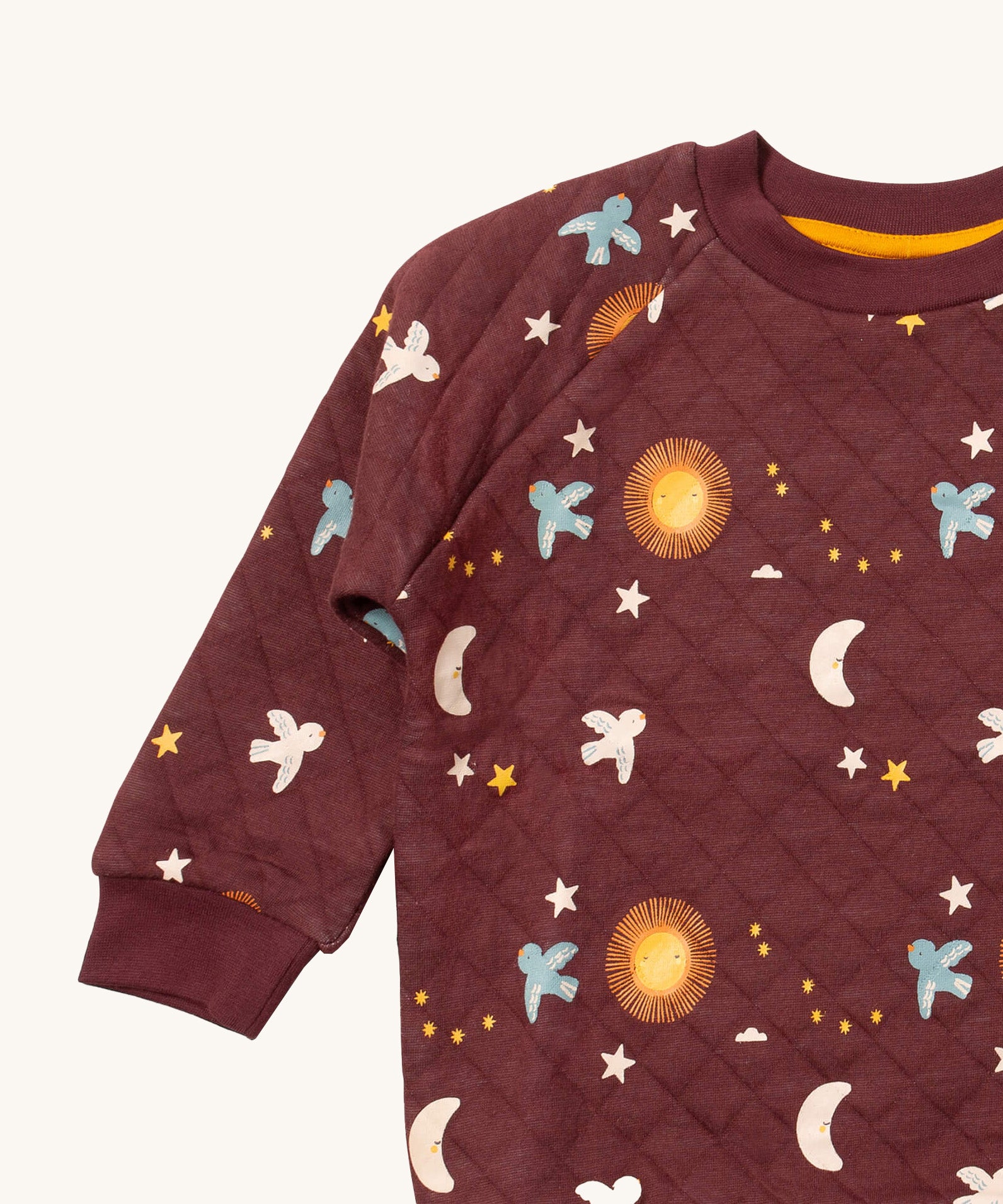 A close up of the Little Green Radicals flying birds quilted sweatshirt that's available at Babipur. Showing the collar and cuff detail dark maroon organic cotton fabric with cute prints of flying birds