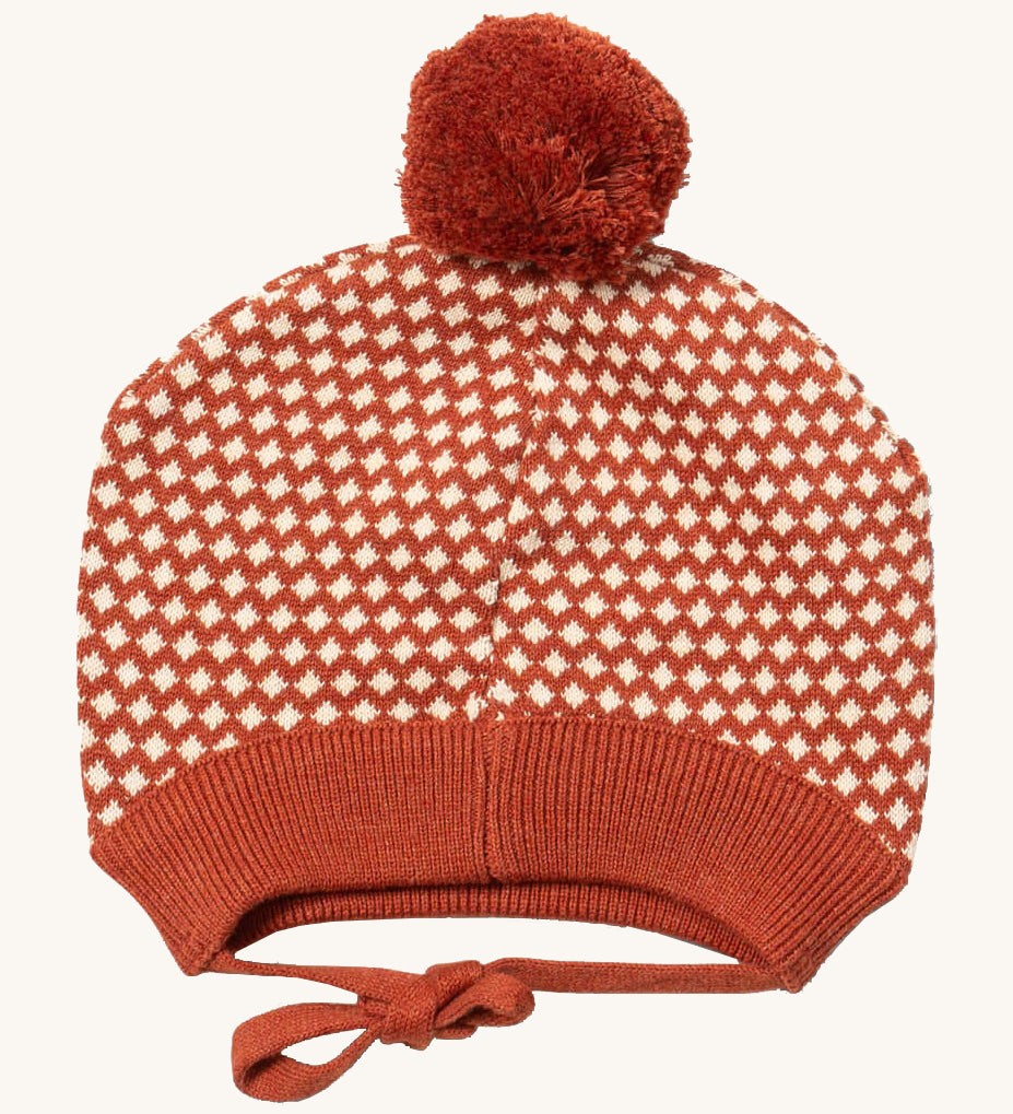 Little Green Radicals ginger diamond knitted beanie hat available at Babipur. A  knitted GOTS organic cotton beanie style hat with a dark orange and cream diamond design and light brown pom pom on top. Features matching dark orange ties for a secure fit.