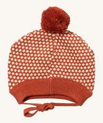 Little Green Radicals ginger diamond knitted beanie hat available at Babipur. A  knitted GOTS organic cotton beanie style hat with a dark orange and cream diamond design and light brown pom pom on top. Features matching dark orange ties for a secure fit.