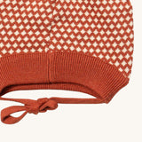 A close up of the Little Green Radicals ginger diamond knitted beanie hat showing the closed dark orange tie detail on organic cotton fabric