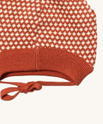 A close up of the Little Green Radicals ginger diamond knitted beanie hat showing the closed dark orange tie detail on organic cotton fabric