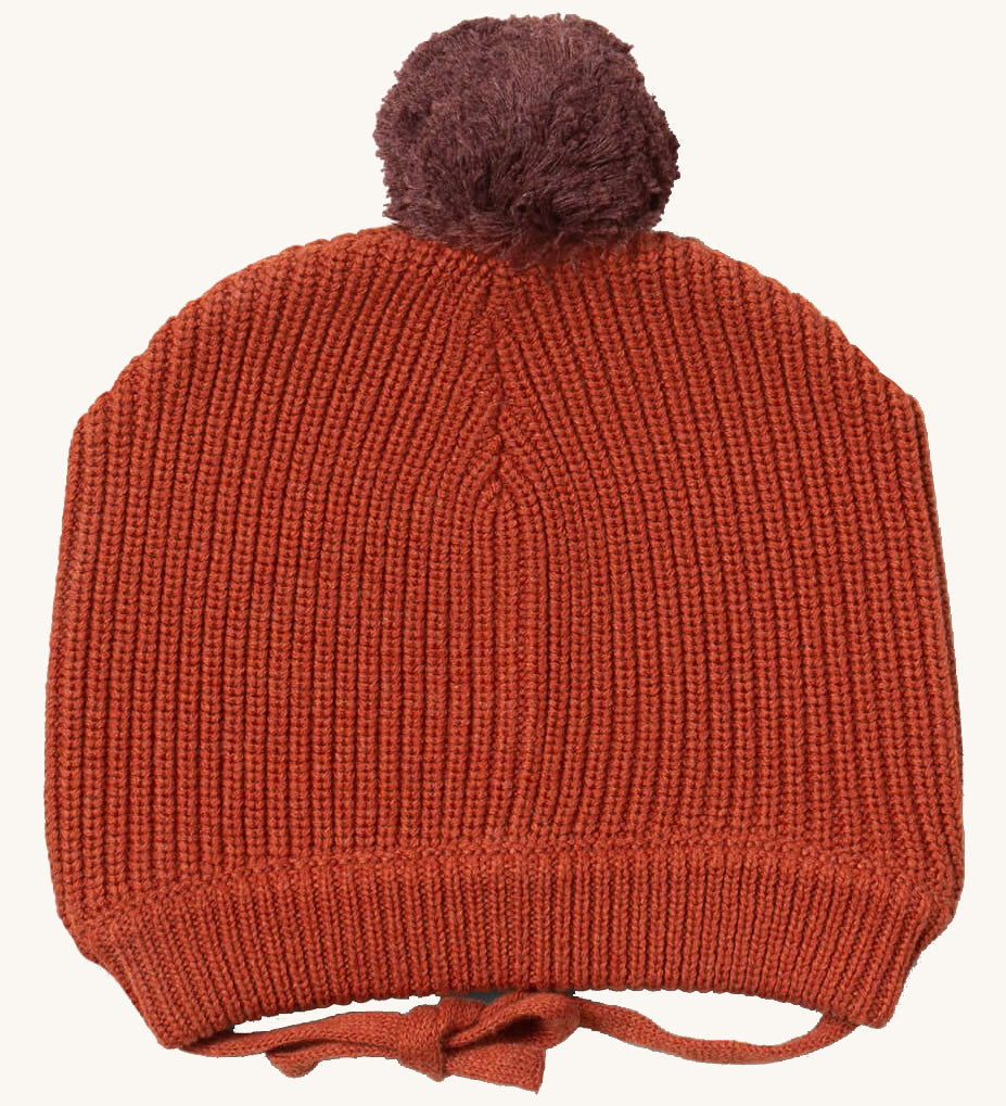 Little Green Radicals ginger knitted beanie hat available at Babipur. A dark orange knitted GOTS organic cotton beanie style hat with a purple pom pom on top. Features matching dark orange ties for a secure fit.