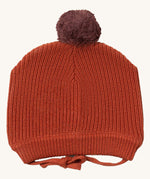 Little Green Radicals ginger knitted beanie hat available at Babipur. A dark orange knitted GOTS organic cotton beanie style hat with a purple pom pom on top. Features matching dark orange ties for a secure fit.