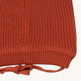 A close up of the Little Green Radicals ginger knitted beanie hat showing the closed dark orange tie detail on organic cotton fabric