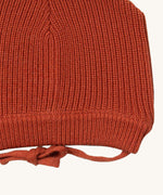 A close up of the Little Green Radicals ginger knitted beanie hat showing the closed dark orange tie detail on organic cotton fabric