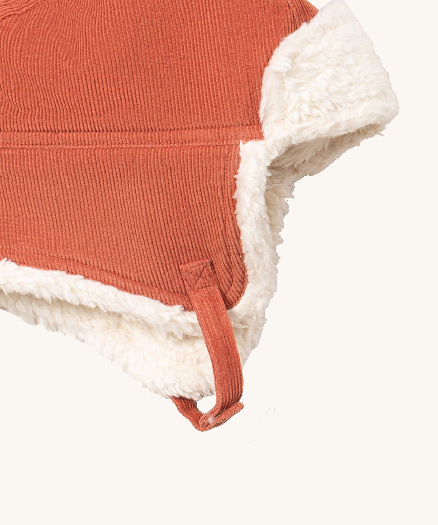 A close up of the Little Green Radials sherpa fleece cosy hat in ginger. Showing the foldable ear flaps, the white sherpa fleece inner and matching corduroy chin strap on dark orange organic cotton fabric