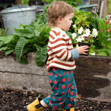 Young child wearing Little Green Radicals ginger striped knitted jumper with repeat apple print trousers and yellow gold wellington boots. 