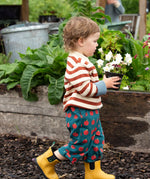 Young child wearing Little Green Radicals ginger striped knitted jumper with repeat apple print trousers and yellow gold wellington boots. 