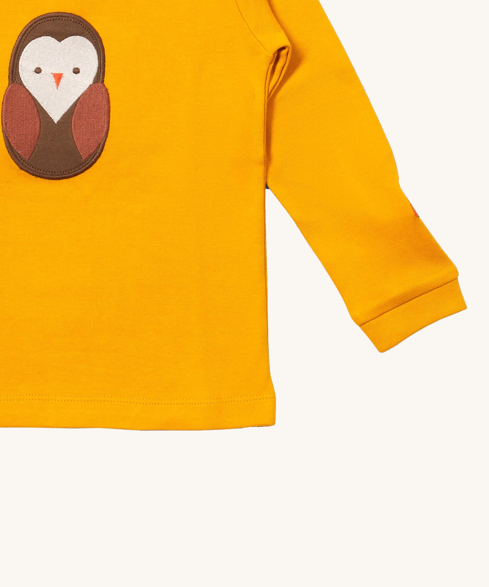 A close up of the Little Green Radicals gold brown owl applique long sleeve top showing the cute brown owl applique and sleeve detail on dark yellow organic cotton fabric