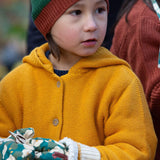 A close up of a child wearing the Little Green Radicals gold snuggly hooded knitted cardigan.Showing the knit detail on yellow organic cotton fabric.