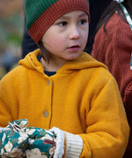 A close up of a child wearing the Little Green Radicals gold snuggly hooded knitted cardigan.Showing the knit detail on yellow organic cotton fabric.