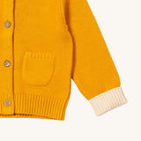 A close up of the Little Green Radicals gold snuggly hooded knitted cardigan. Showing the knitted pocket and cream cuff detail on yellow organic cotton fabric.