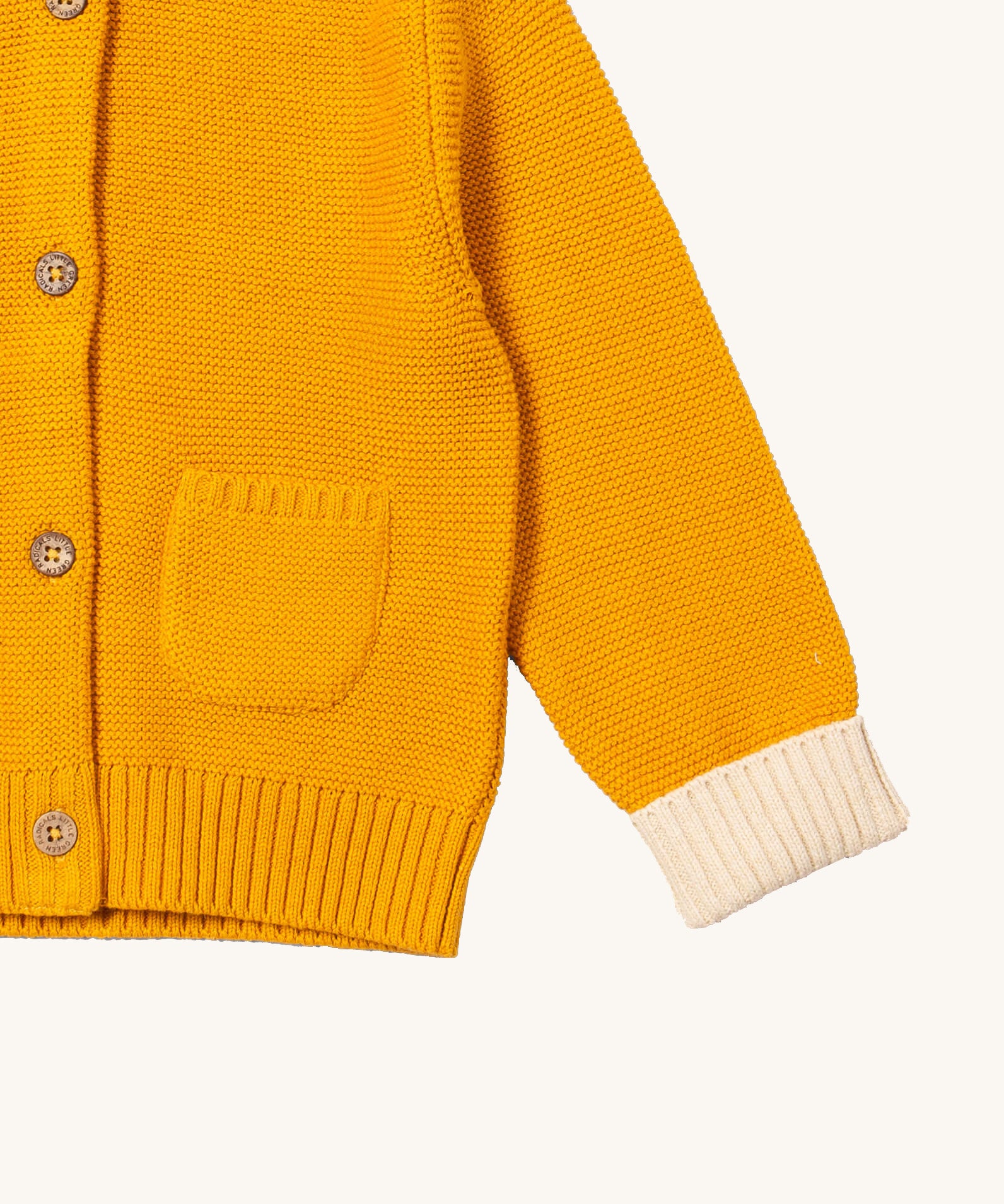 A close up of the Little Green Radicals gold snuggly hooded knitted cardigan. Showing the knitted pocket and cream cuff detail on yellow organic cotton fabric.