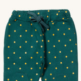 A close up the Little Green Radicals golden stars cosy joggers showing the drawstring detail, 2 side pockets and stitched on knee patches  on dark turquoise organic cotton fabric.