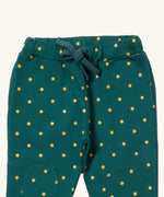 A close up the Little Green Radicals golden stars cosy joggers showing the drawstring detail, 2 side pockets and stitched on knee patches  on dark turquoise organic cotton fabric.