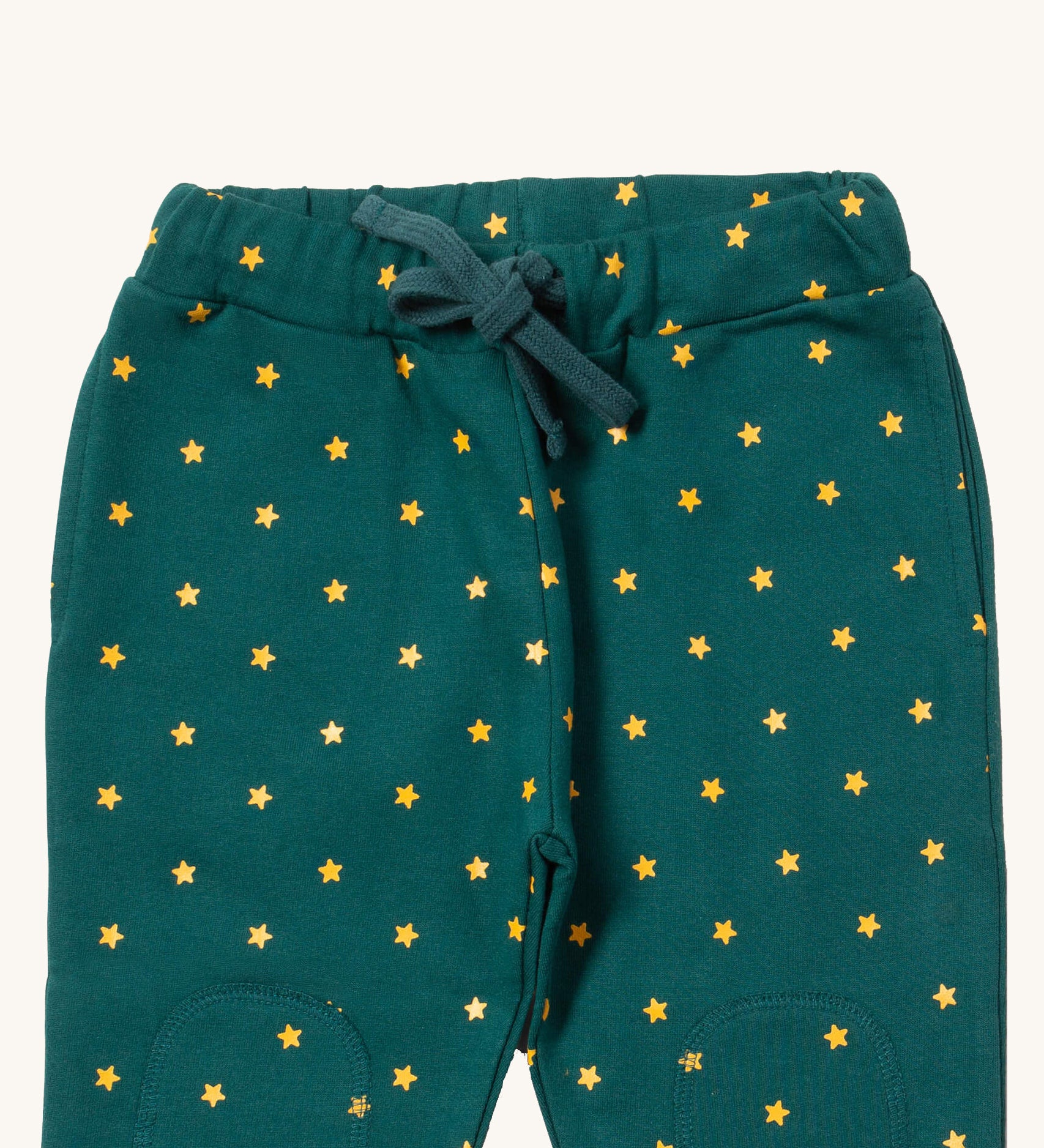 A close up the Little Green Radicals golden stars cosy joggers showing the drawstring detail, 2 side pockets and stitched on knee patches  on dark turquoise organic cotton fabric.