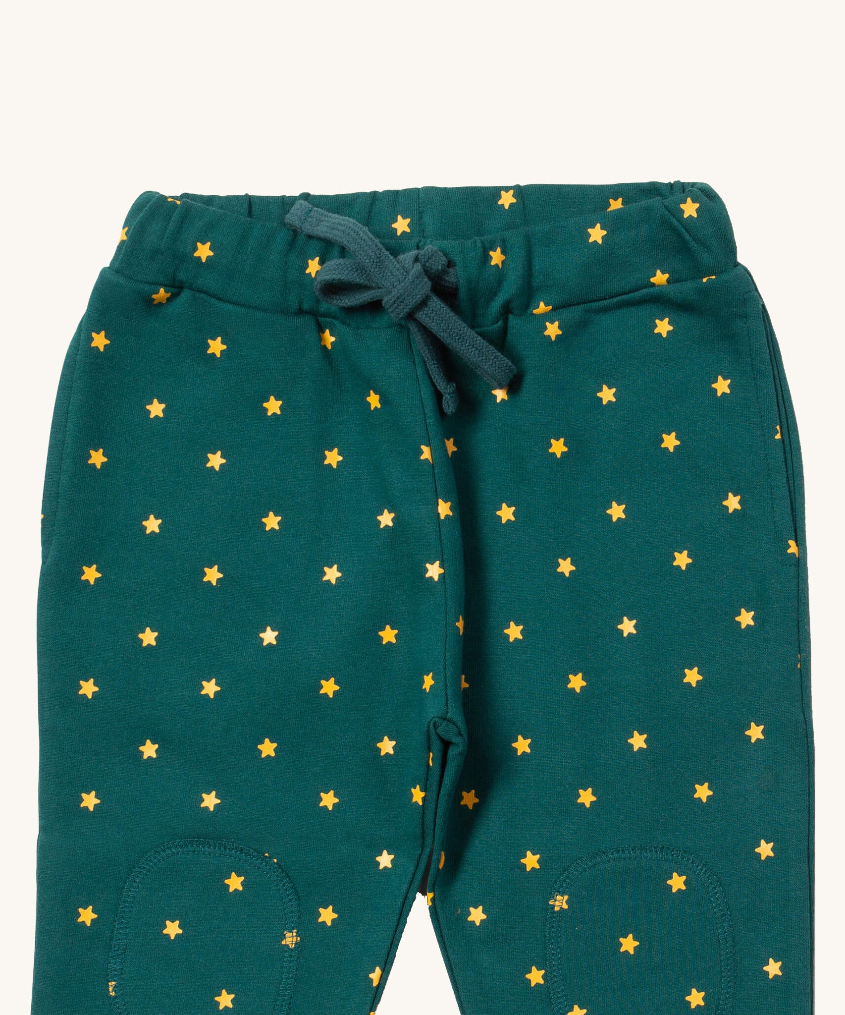 A close up the Little Green Radicals golden stars cosy joggers showing the drawstring detail, 2 side pockets and stitched on knee patches  on dark turquoise organic cotton fabric.