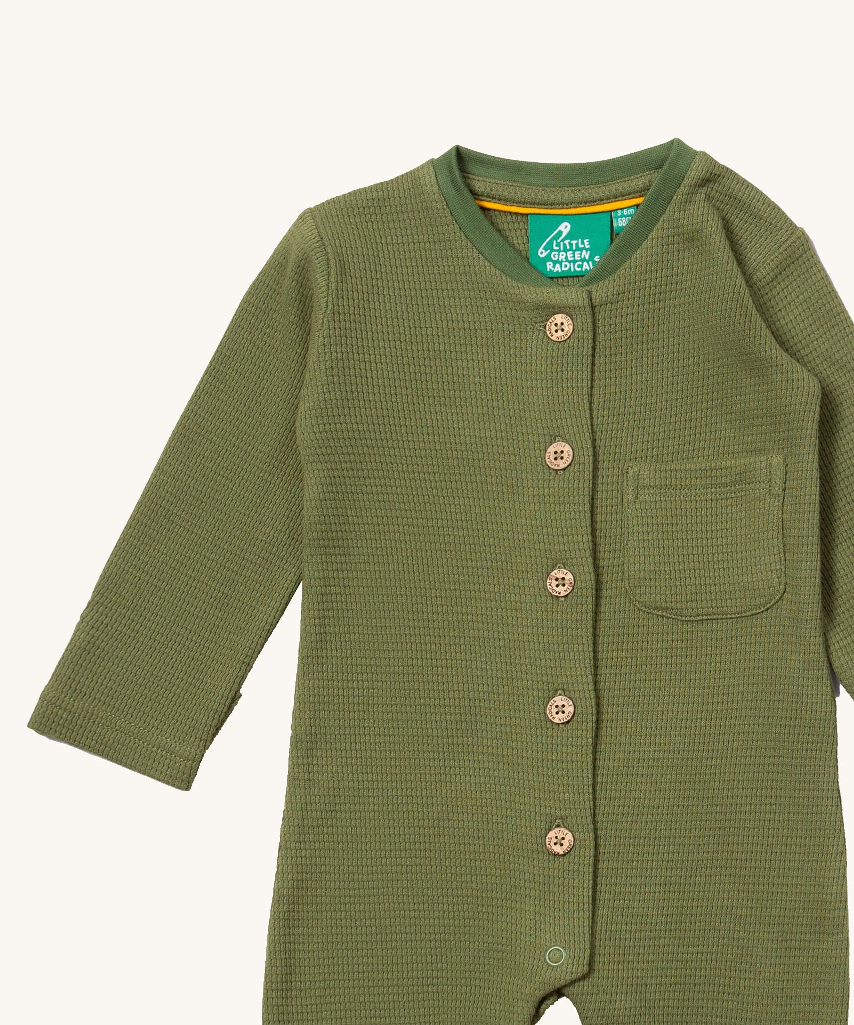 A close up of the Little Green Radicals green chive waffle playsuit showing the button fastener detail and waffle knit detail. 