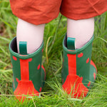 A child wearing the Little Green Radicals kid wellington boots showing the length of the boots and pull on tab detail on the back of the boots. 