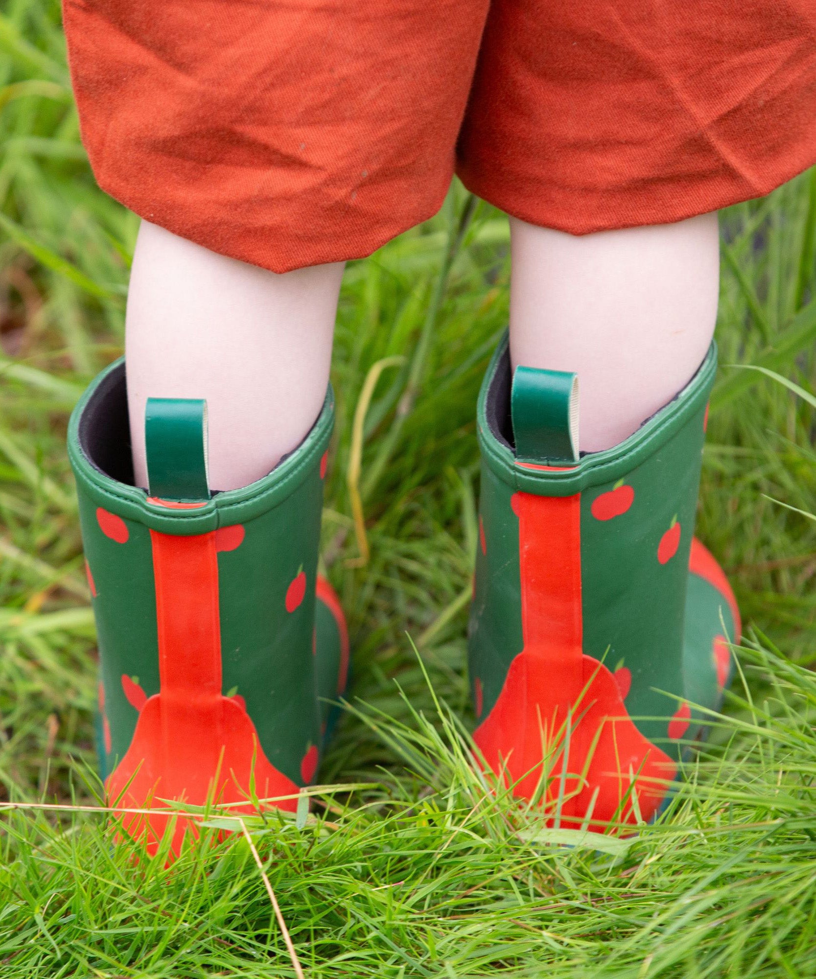 A child wearing the Little Green Radicals kid wellington boots showing the length of the boots and pull on tab detail on the back of the boots. 