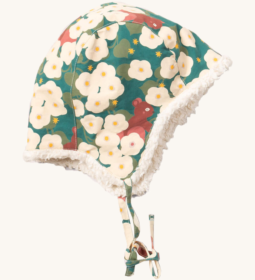 Little Green Radials sherpa fleece lined hat in hedgehrow. A GOTS organic cotton turquoise hat with turn up ear flaps and a white sherpa style fleece inner. Features a matching hedgerow print tie for a secure fit