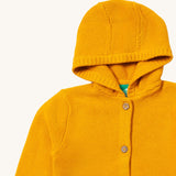 A close up of the Little Green Radicals gold snuggly hooded knitted cardigan. Showing the generous hood detail and button fasteners down the middle yellow organic cotton fabric.