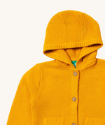 A close up of the Little Green Radicals gold snuggly hooded knitted cardigan. Showing the generous hood detail and button fasteners down the middle yellow organic cotton fabric.
