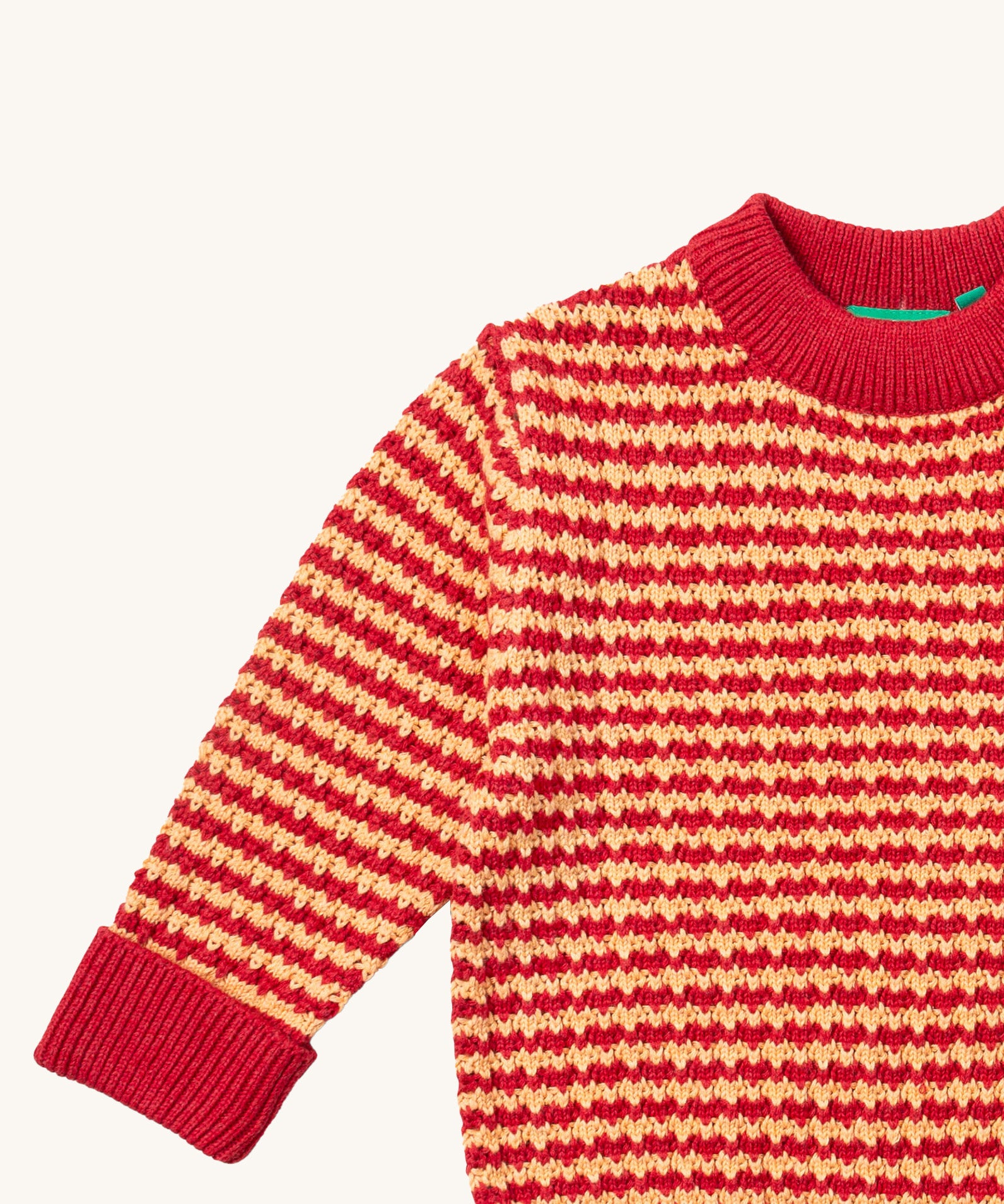 A close up of the Little Green Radicals snuggly knitted jumper in juniper stripe. Showing the yellow and pale red stripe knit detail and the matching pale red collar and turned up cuff