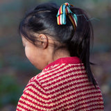 A child wearing the Little Green Radicals snuggly knitted jumper in juniper stripe. Showing the knitted detail and pale red collar on striped GOTS organic cotton fabric available a at Babipur.