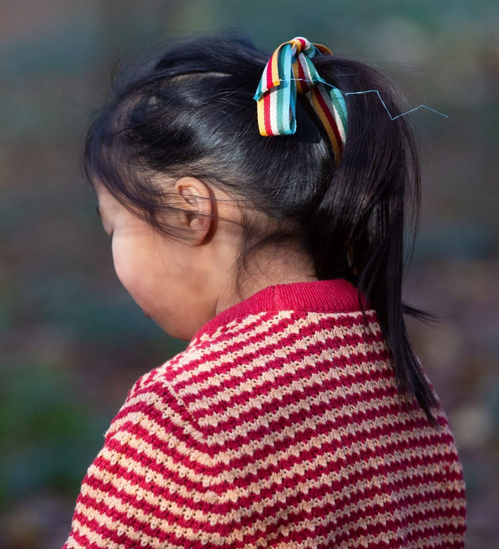 A child wearing the Little Green Radicals snuggly knitted jumper in juniper stripe. Showing the knitted detail and pale red collar on striped GOTS organic cotton fabric available a at Babipur.