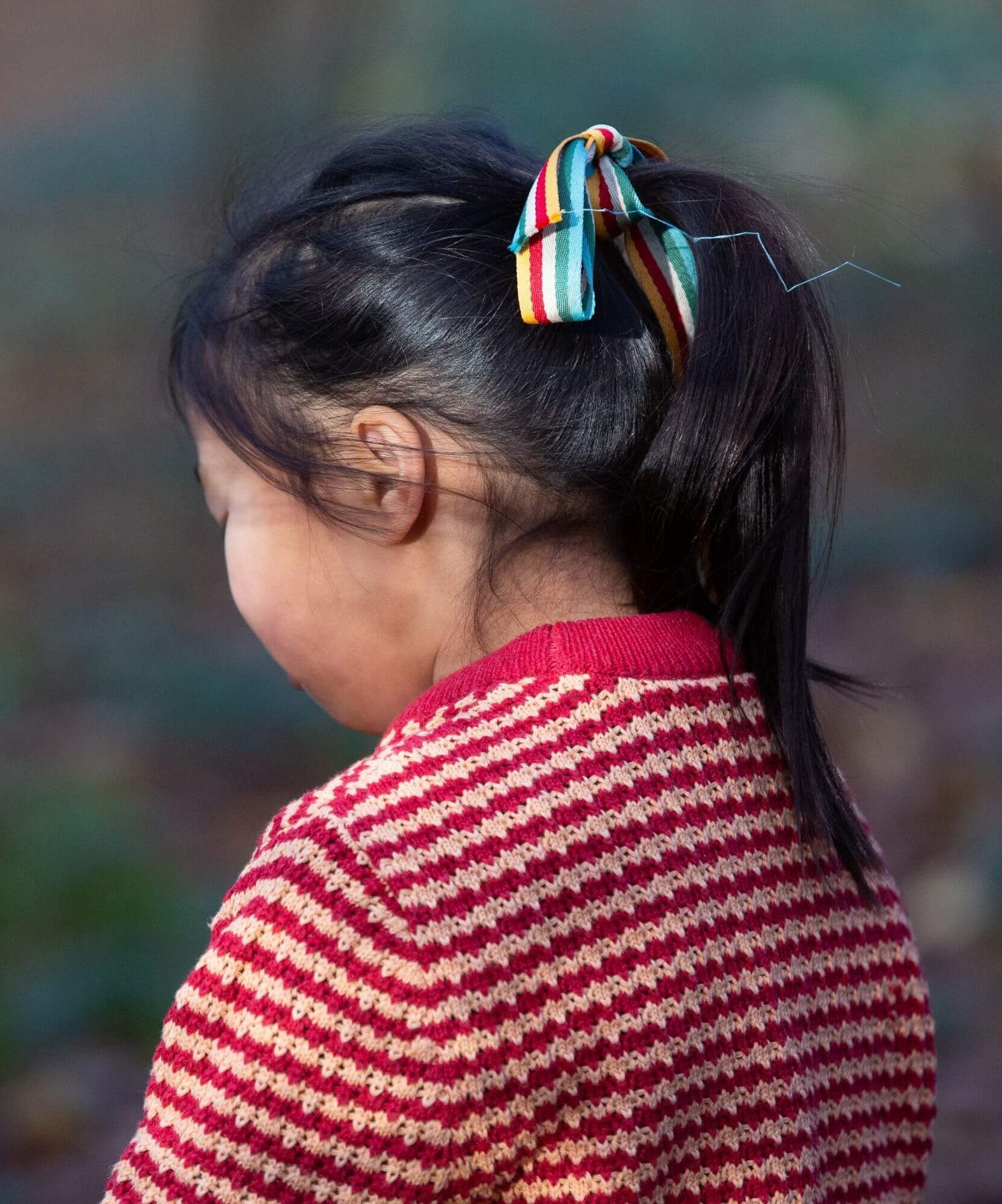 A child wearing the Little Green Radicals snuggly knitted jumper in juniper stripe. Showing the knitted detail and pale red collar on striped GOTS organic cotton fabric available a at Babipur.