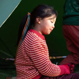 A child wearing the Little Green Radicals snuggly knitted jumper in juniper stripe. Showing the knit detail and pale red trim on yellow and pale red striped GOTS organic cotton fabric available at Babipur.