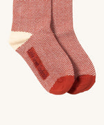 A close up of the red and white striped Little Green Radicals ankle socks showing zig zag stripe detail and brand name on the sole on soft brown organic cotton fabric