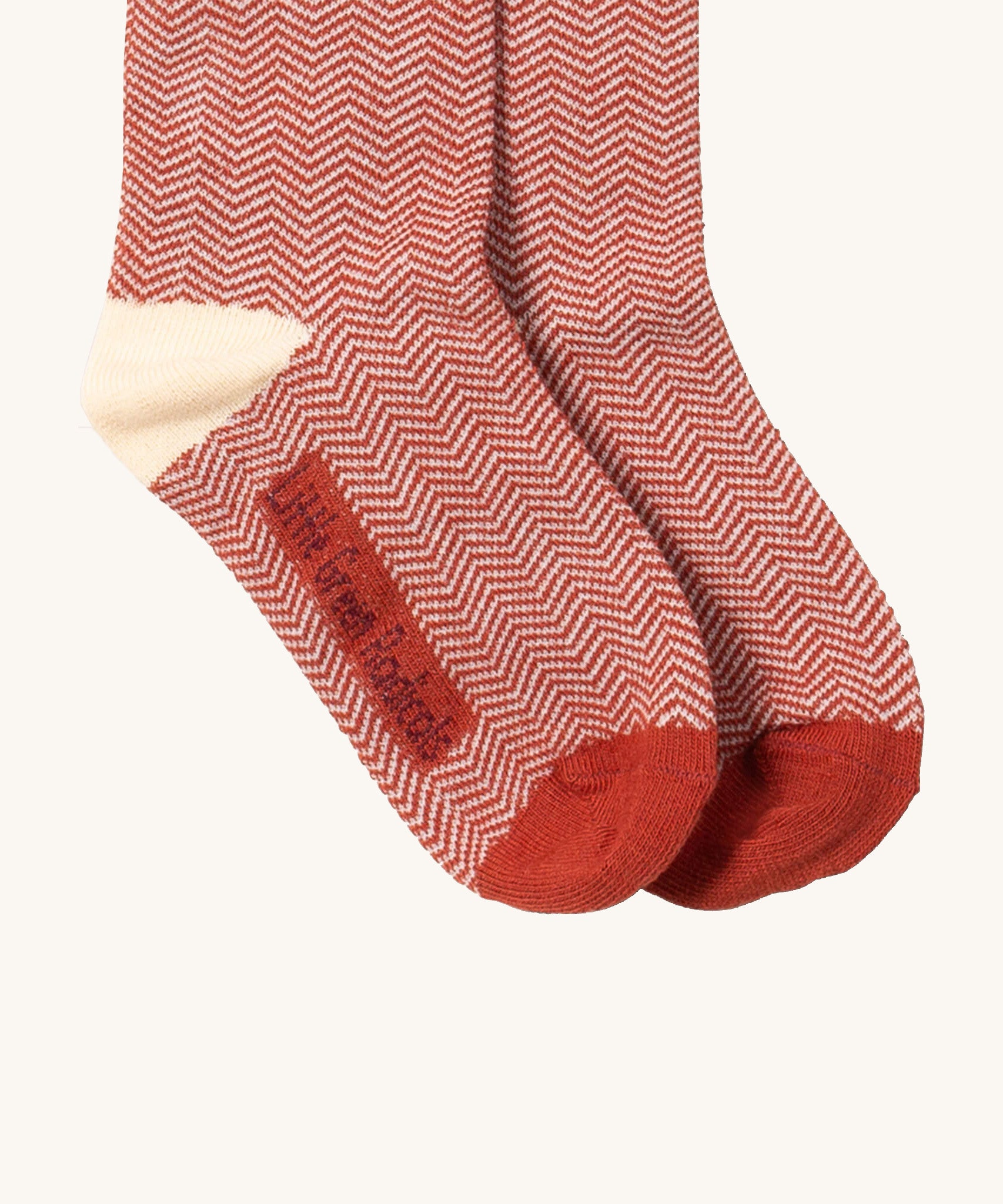 A close up of the red and white striped Little Green Radicals ankle socks showing zig zag stripe detail and brand name on the sole on soft brown organic cotton fabric