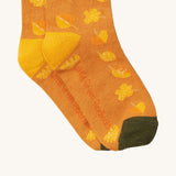 A close up of the golden leaves Little Green Radicals ankle socks showing autumn inspired yellow leaves design with yellow and green trim with the brand name on the sole on soft organic cotton fabric