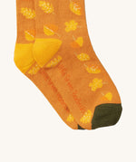 A close up of the golden leaves Little Green Radicals ankle socks showing autumn inspired yellow leaves design with yellow and green trim with the brand name on the sole on soft organic cotton fabric