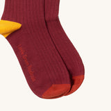 A close up of the maroon block coloured Little Green Radicals ankle socks showing the yellow and red trim and brand name on the sole on soft organic cotton fabric