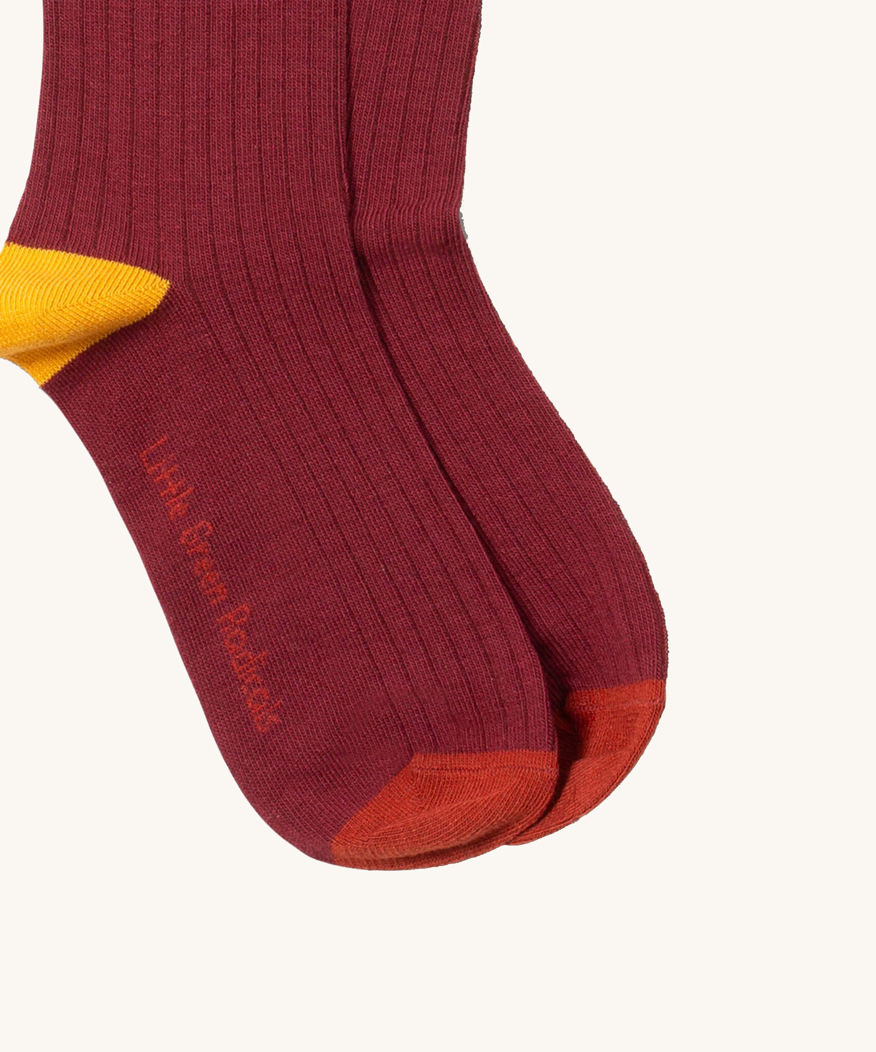 A close up of the maroon block coloured Little Green Radicals ankle socks showing the yellow and red trim and brand name on the sole on soft organic cotton fabric