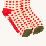 A close up of the red and white checked Little Green Radicals ankle socks check detail with red and green trim with the brand name on the sole on organic cotton fabric.