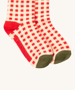 A close up of the red and white checked Little Green Radicals ankle socks check detail with red and green trim with the brand name on the sole on organic cotton fabric.