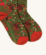 A close up of the Little Green Radicals winter rabbit ankle socks. Showing the rabbit design detail and red trim with the brand name on the the sole on dark green organic cotton fabric.
