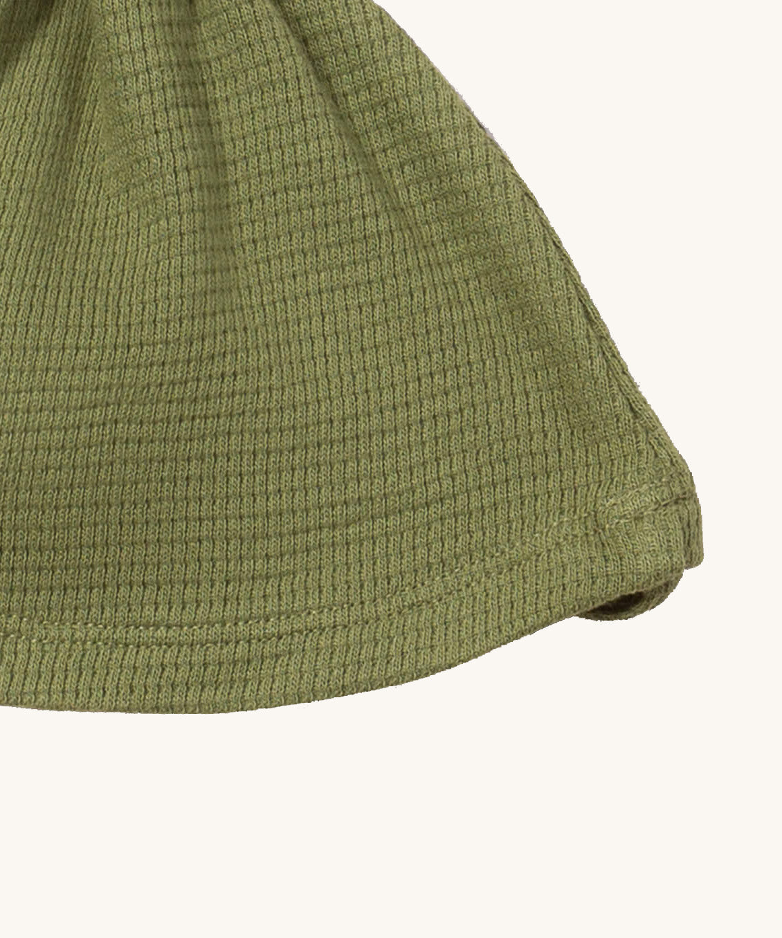 A close up of the Little Green Radicals chive waffle tie hat showing waffle knit detail on green organic cotton fabric