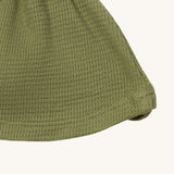A close up of the Little Green Radicals chive waffle tie hat showing waffle knit detail on green organic cotton fabric