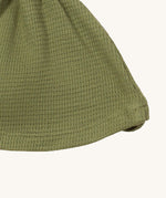 A close up of the Little Green Radicals chive waffle tie hat showing waffle knit detail on green organic cotton fabric