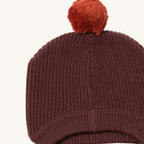 A close up of the Little Green Radicals chocolate knitted beanie hat showing the knit detail and light brown pom pom on stitched brown organic cotton fabric.