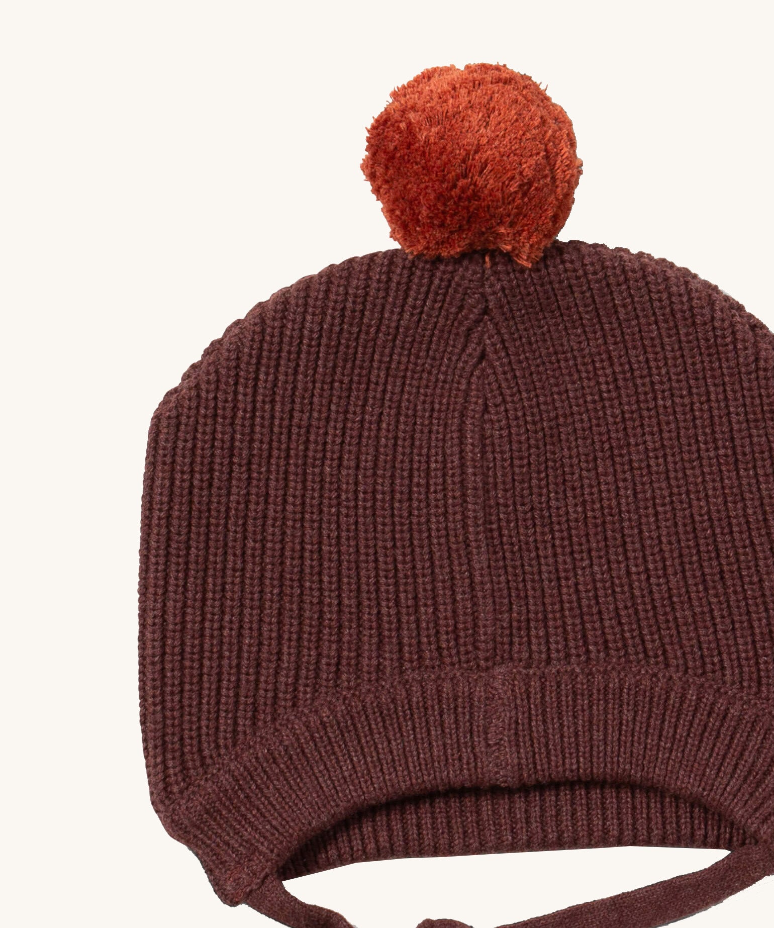A close up of the Little Green Radicals chocolate knitted beanie hat showing the knit detail and light brown pom pom on stitched brown organic cotton fabric.