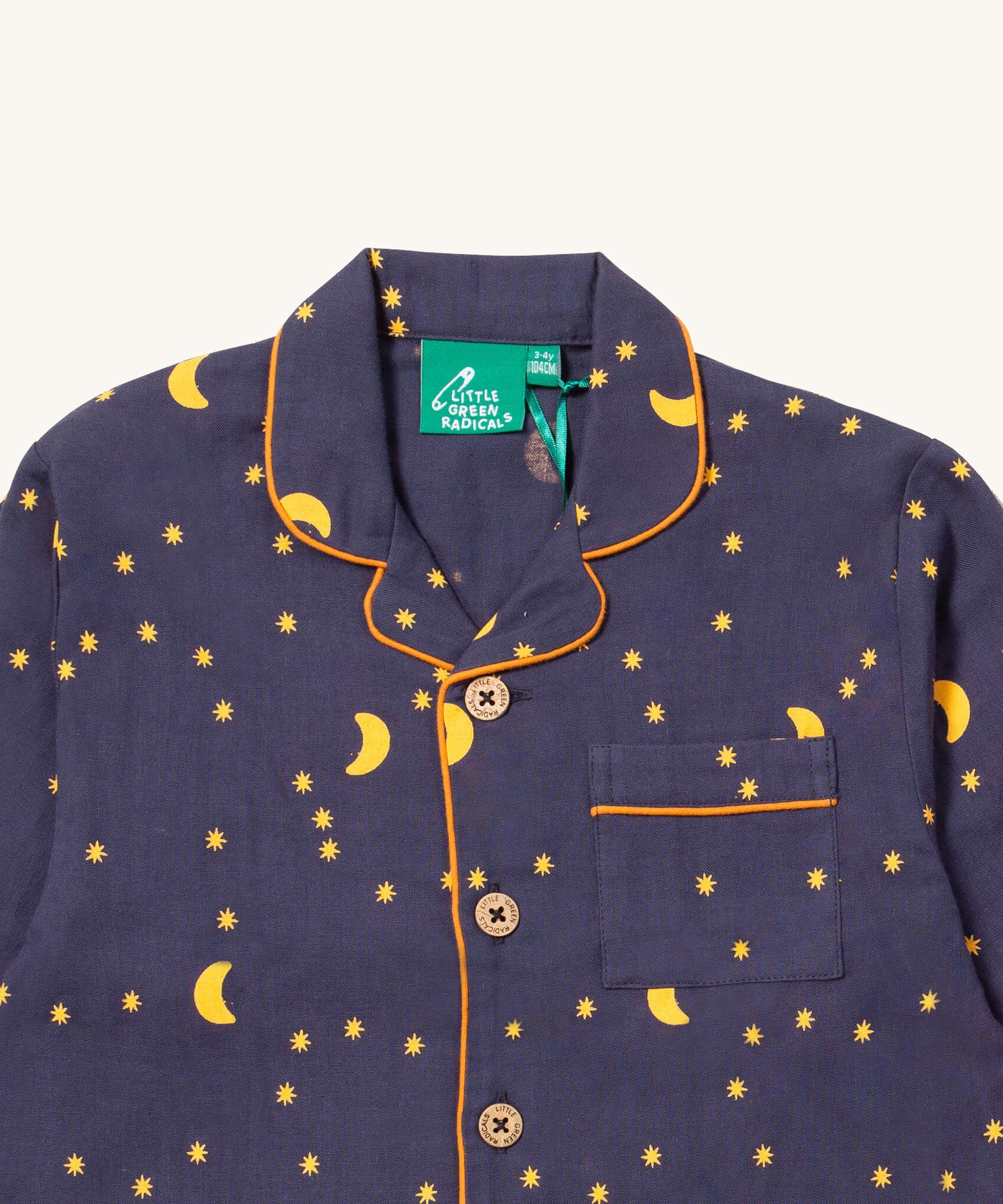 A close up of the Little Green Radicals classic pyjama top from the dark night classic set. showing the yellow trim detail around the collar and pocket. Showing a close up of the starry night print detail and button fasteners on navy organic cotton fabric
