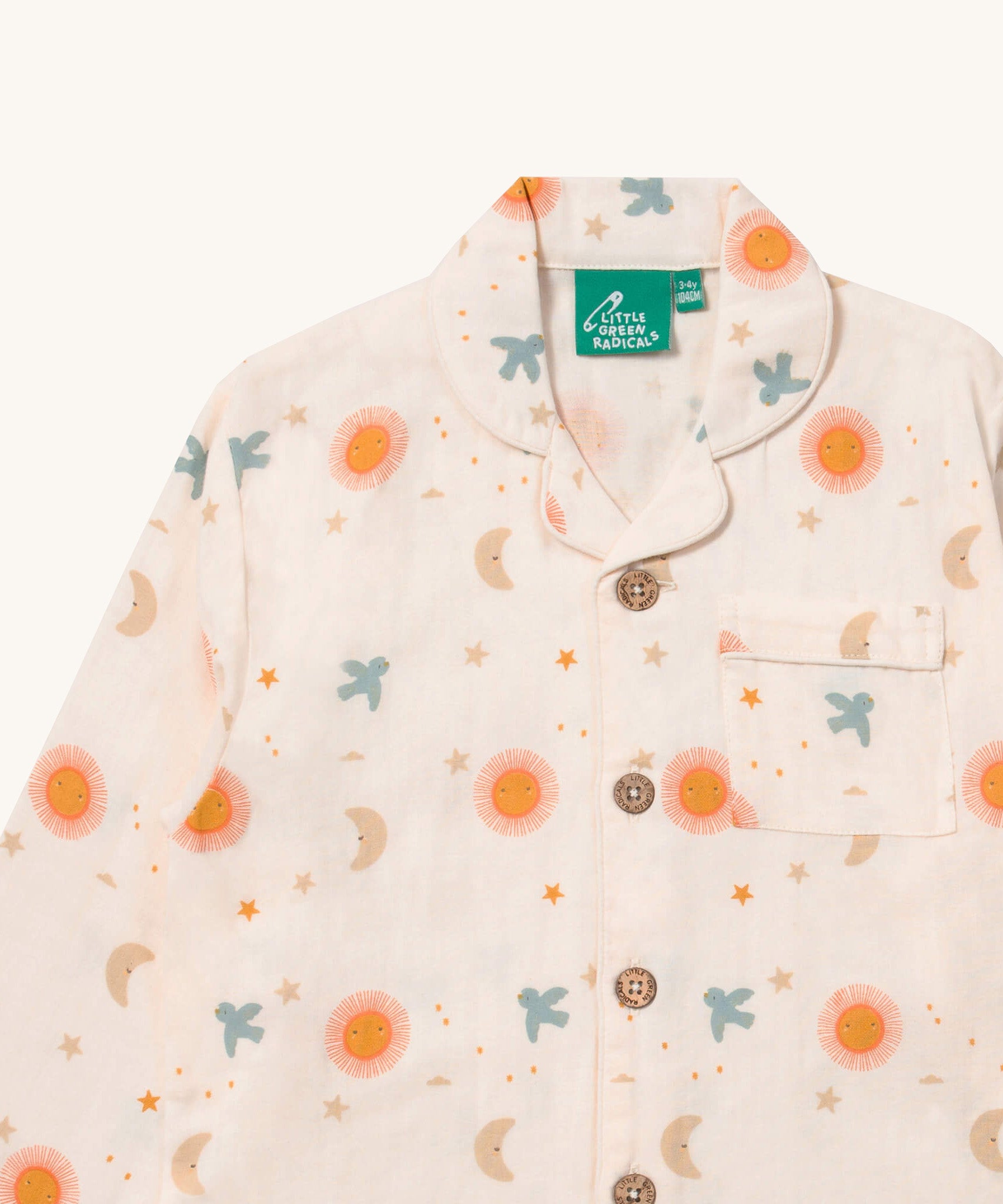 A close up of the Little Green Radicals classic pyjama top from the moon and sun set showing the collar and pocket detail on with the button fasteners running down the middle of the light pink organic cotton top