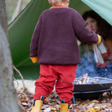 A child walking through leaves in a woodland and wearing the Little Green Radicals comfy corduroy trousers in ginger with the navy sheep knitted jumper.  A corduroy style trouser that's loose fitted in dark orange organic cotton fabric