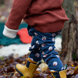 A child walking though leaves in a woodland wearing the Little Green Radicals comfy joggers in sleeping sheep. A navy jogger with cute prints of sheep on soft GOTS organic cotton fabric